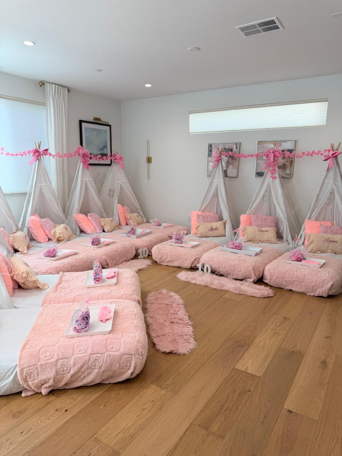 Wide view of a pink teepee slumber party with floor beds and a floral garland